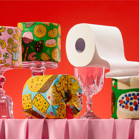 Stacks of colourful 'Who Gives a Crap' Sweet Limited Edition toilet paper rolls arranged on top of glasses.